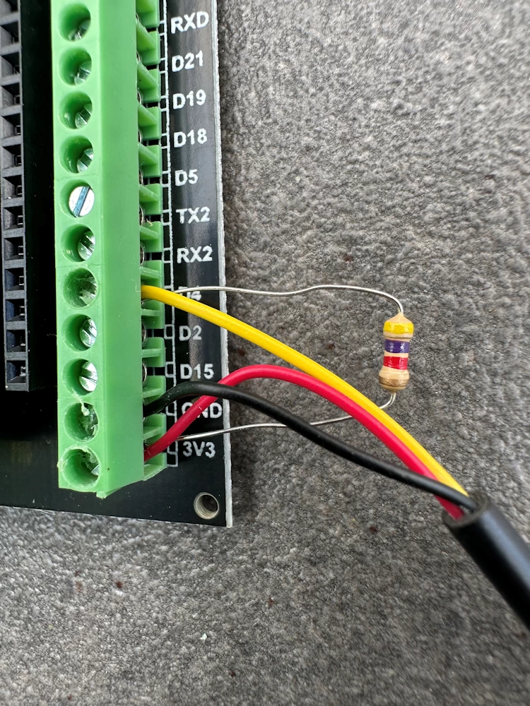 Nahaufnahme der Verkabelung eines DS18B20 Temperatursensors an den grünen Schraubklemmen des ESP32 Breakout-Boards mit dem 4,7 kOhm Pull-up-Widerstand