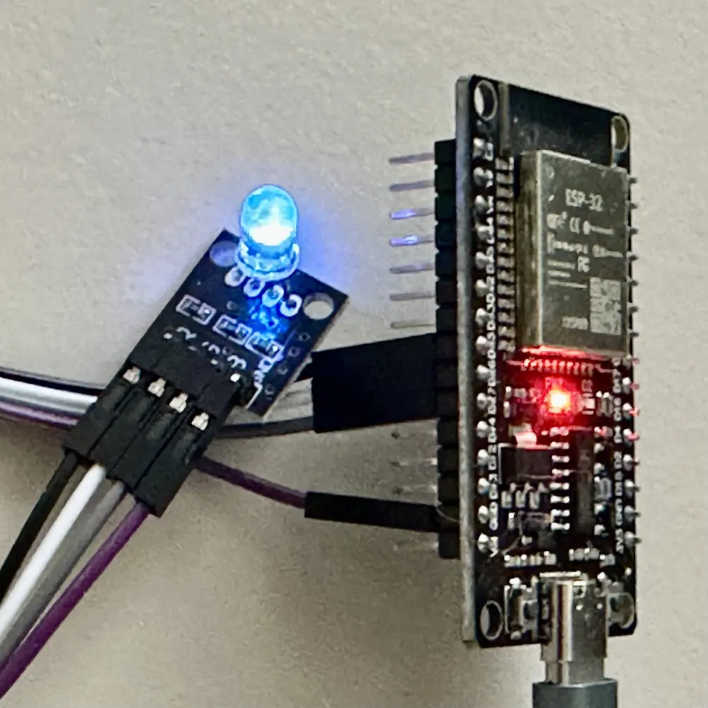 Nahaufnahme eines ESP32-Mikrocontrollers, der über Jumper-Kabel mit einem aktiv blau leuchtenden KY-016 RGB-LED-Modul verbunden ist